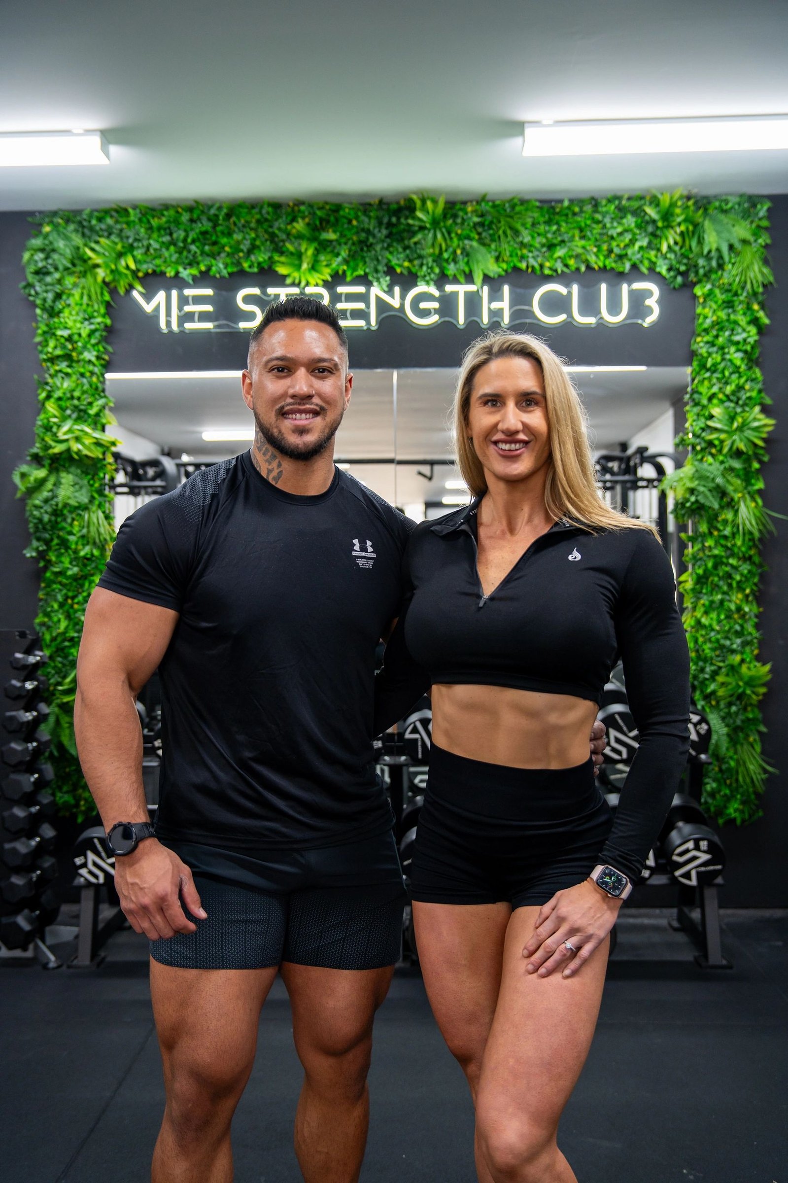 Founders Mak and Ellie in front of the green M|E Strength Club wall